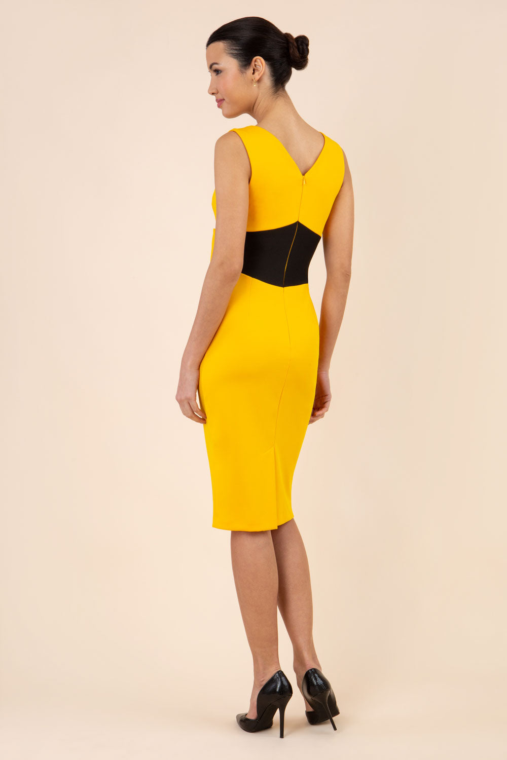 blonde model wearing Diva Catwalk Pencil sleeveless dress with rounded neckline and bow detail at the front with a contrasting black band in saffron yellow back