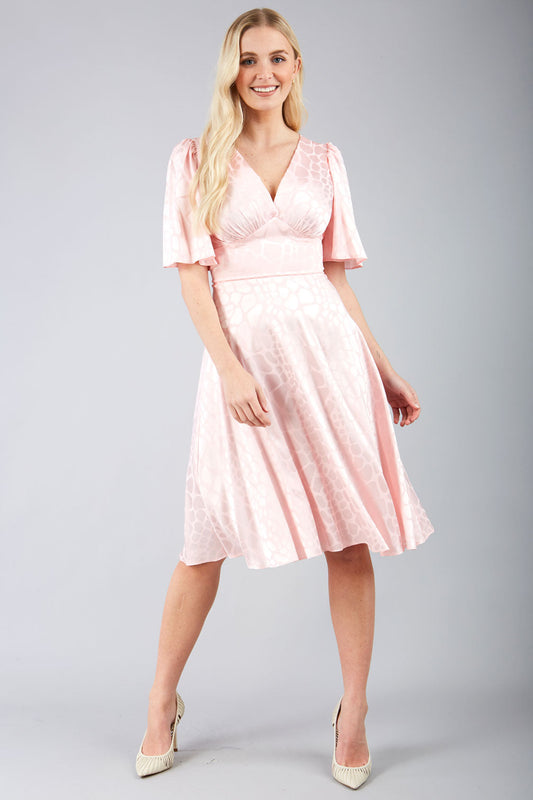 model wearing diva catwalk cambrian satin swing dress with bell short sleeve wide asymmetric waistband and pleating under bust in pink front